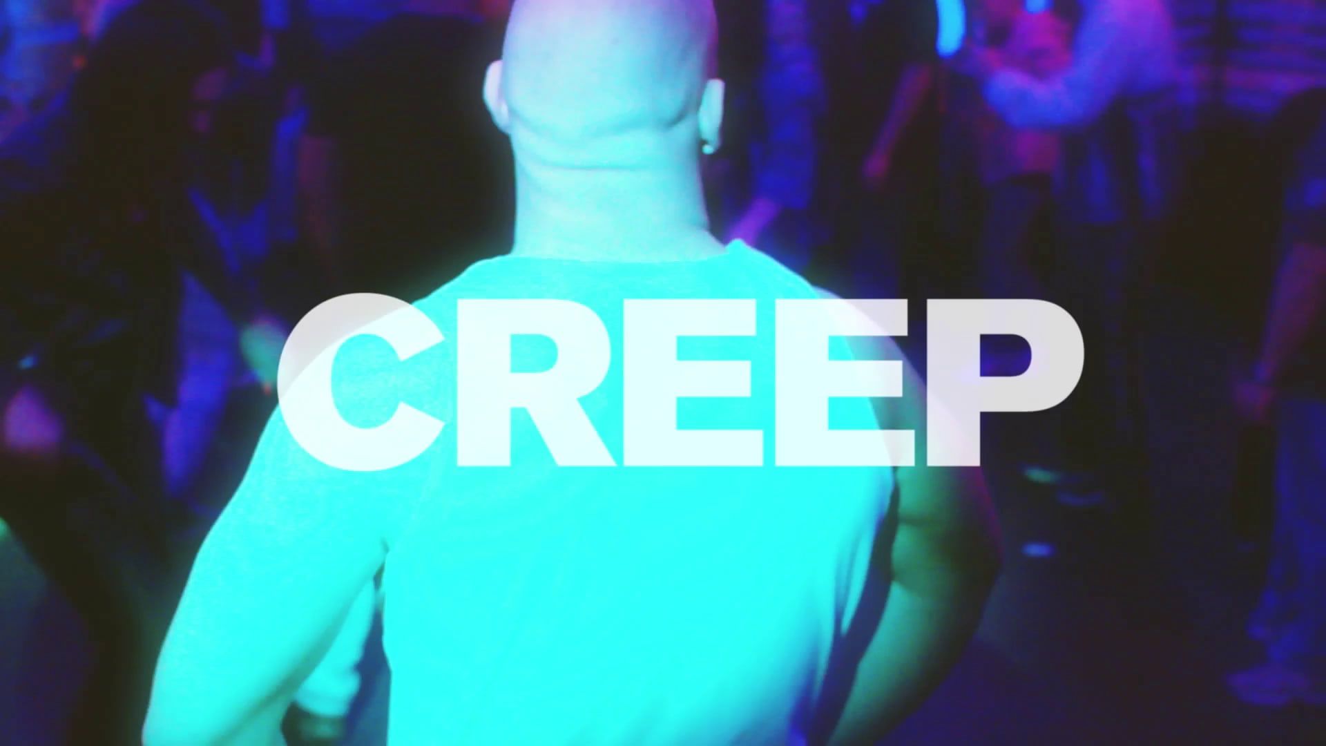 A man seen from behind in a turquoise-lit crowd, the word CREEP across his shoulders.