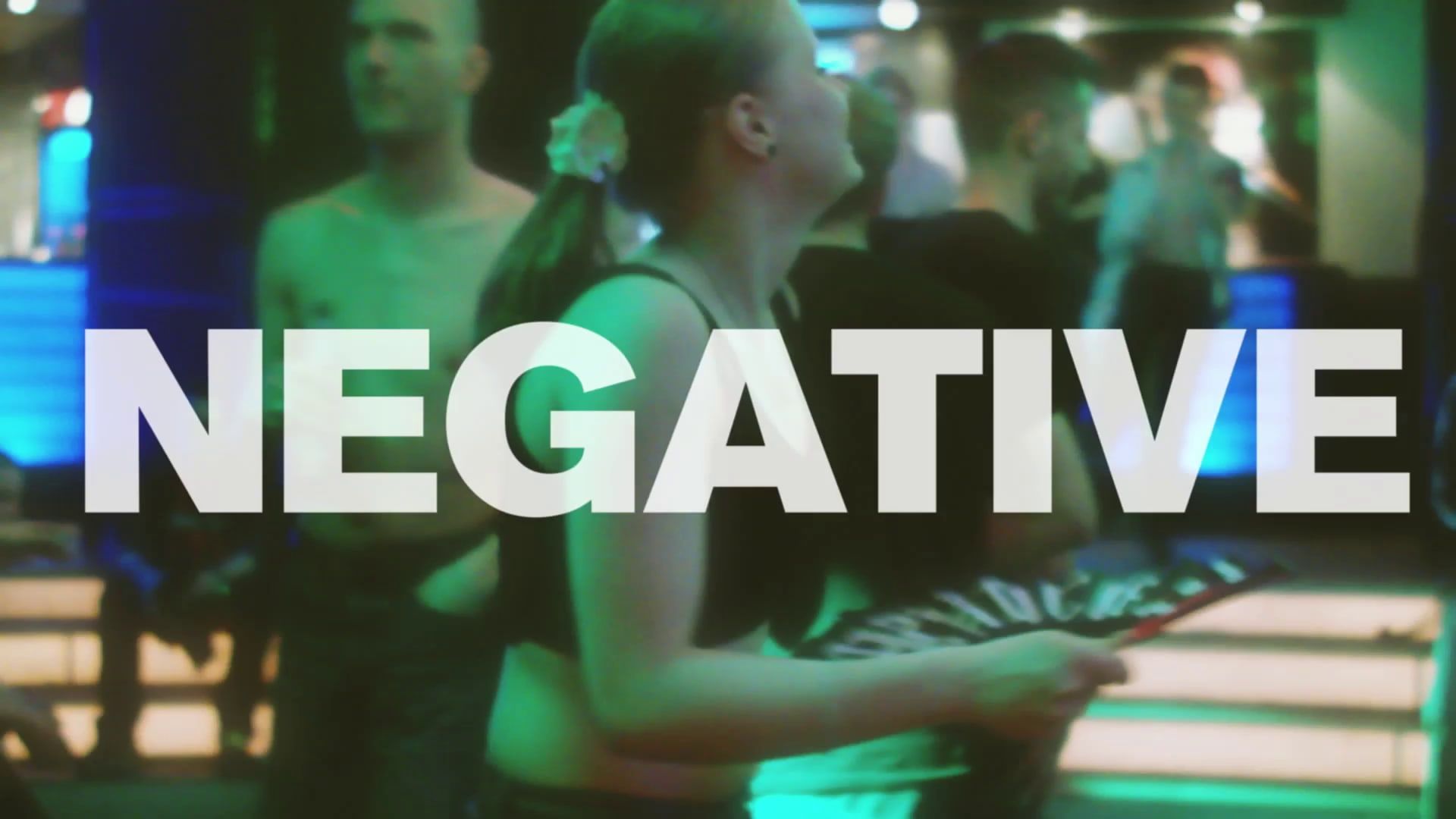 A dancer in a black crop top tilts her head back under green club light, the word NEGATIVE across the frame.